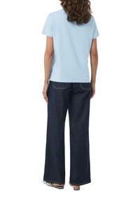 Jasnoniebieska, krótko rękawowa koszulka w połączeniu z szerokimi, ciemnoniebieskimi dżinsami. Koszulka jest gładka, natomiast dżinsy mają kontrastowe szwy.