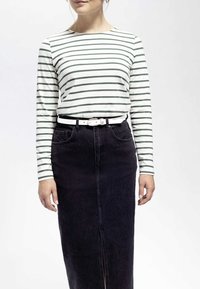 Langärmliges, weißes Hemd mit grünen horizontalen Streifen, kombiniert mit einem schwarzen Jeansrock und einem weißen Gürtel. Schlichtes, tailliertes Design.