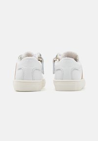 Sneaker bianchi con dettagli color cammello, suole testurizzate e rivestimento morbido. Presentano una cerniera posteriore e lacci piatti per una vestibilità sicura e una facile indossabilità.