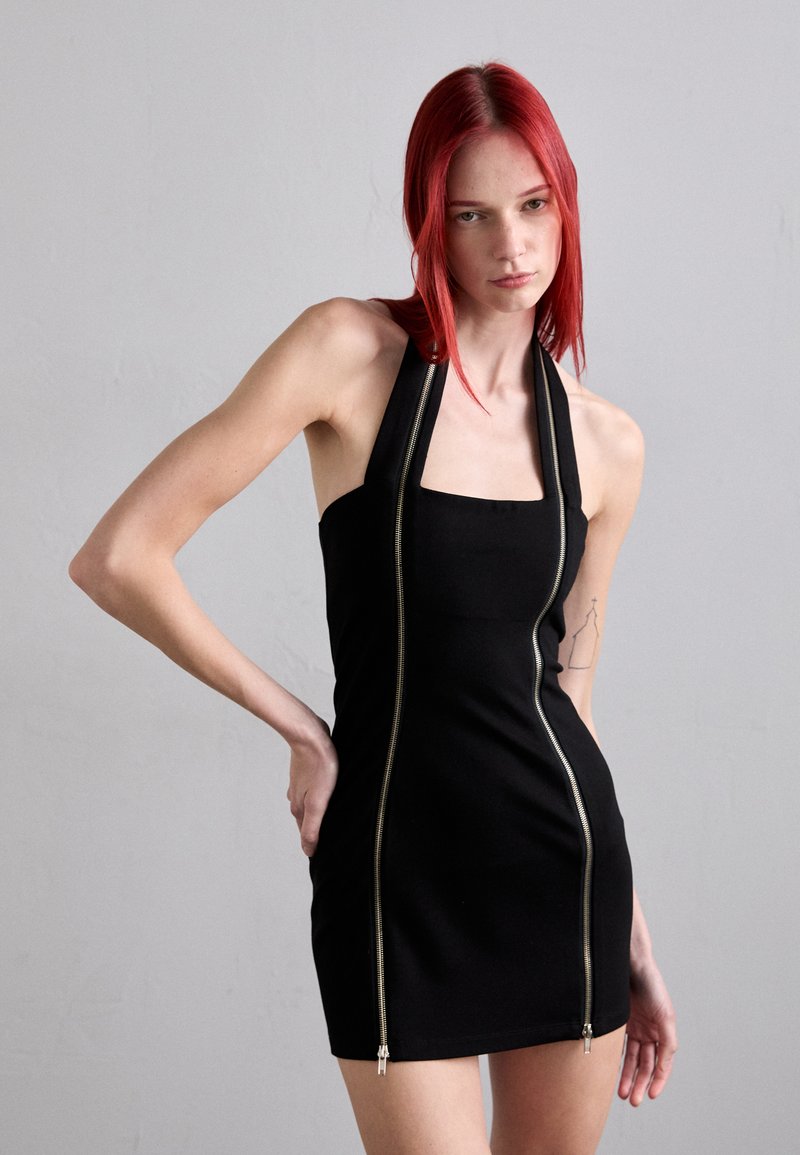 Miniabito nero a halter realizzato in materiale elasticizzato, con due zip frontali e scollatura quadrata. Texture liscia, design aderente.