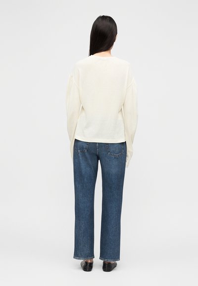 Krem pulover s napihnjenimi rokavi, kombiniran z modrimi ravnimi kavbojkami z zadnjimi žepi in rahlo raztrganim robom.