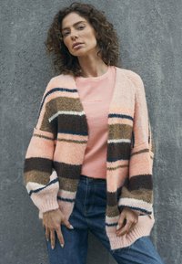 Knitted cardigan with pink, brown, and cream stripes, open-front design, paired with a light pink t-shirt and blue jeans. Soft texture.