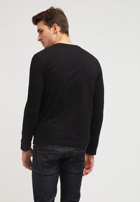 Sort langærmet skjorte lavet af glat bomuld, med rund halsudskæring og en afslappet pasform, parret med mørke denim jeans.