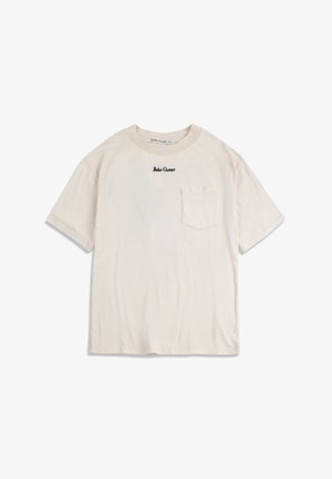 Bež kratka majica s kratkim rukavima, prednjim džepom i crnim logotipom "Bobo Choses" smještenim ispod ovratnika.