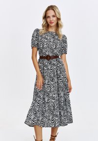 Modelka pozując w sukience w czarno-białe paski zebry z bufkami i brązowym paskiem, prezentuje stylowy, nowoczesny look.
