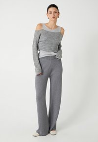 Grå strikket sweater med kold skulder og lange ærmer, parret med løstsiddende grå bukser. Begge lavet af blødt, tekstureret stof.