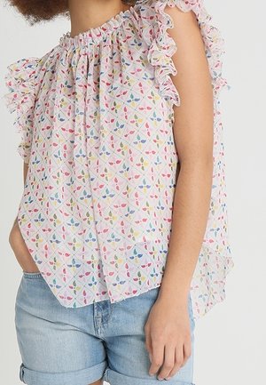 Woman wearing a sleeveless, ruffled, pastel floral blouse paired with light blue rolled-up denim shorts.