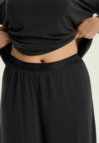 Czarny komplet odzieży domowej z luźną bluzką i spodniami z elastycznym pasem. Miękki materiał o gładkiej fakturze z dyskretnym logo.