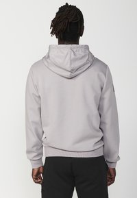Felpa grigia chiara realizzata in morbido tessuto, con cappuccio regolabile tramite coulisse, polsini a coste e un design semplice senza loghi visibili.