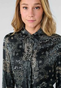 Zwarte knoop-overhemd met paisley- en bloemmotieven in tinten van crème en bruin, voorzien van een kraag en lange mouwen. Glad van textuur.