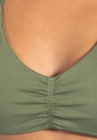 Olijfgroen cropped top met een diepe V-rugontwerp, voorzien van plooidetail in het midden en een gladde, gestructureerde stof.