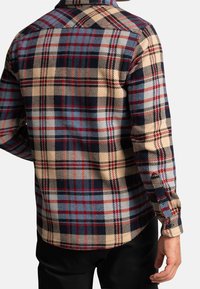 Koszula w kratę z guzikami, w beżowo-granatowo-czerwonej kolorystyce, z teksturowanym materiałem i długimi rękawami. Klasyczny wzór kołnierzyka.
