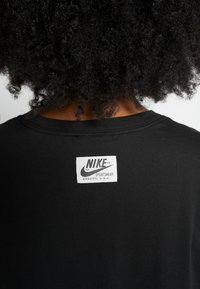 Černé bavlněné tričko s bílou textilní nášivkou na zadní straně, na které je černě vytištěno "NIKE" a "SPORTSWEAR OREGON, U.S.A.".
