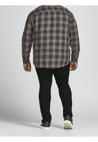 Tummansininen ja khaki ruudullinen pitkähihaisia paita, jossa on napillinen kaulus, yhdistettynä mustiin housuihin ja valkopohjaisiin lenkkareihin.