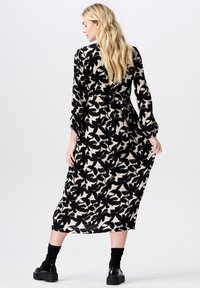 Zwart en beige bloemenmaxi-jurk met lange mouwen en een cinched taille. Textuurstof met grote zwarte bladenpatronen.