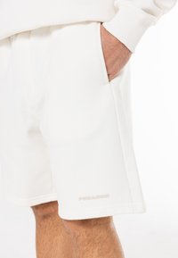 Short en mélange de coton blanc à coupe décontractée, avec poches latérales et un discret logo "PEGADOR" près de l'ourlet droit. Texture lisse.