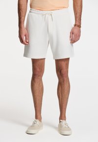 Hvide bomulds shorts med elastisk talje og snøre. Har sidelommer og en afslappet pasform, båret med lyse sneakers.