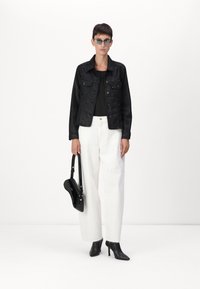 Giubbotto di denim nero su un top nero, abbinato a pantaloni bianchi a gamba larga, stivali neri con tacco e una borsa nera con tracolla.