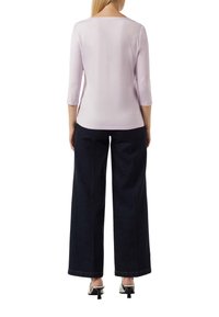 Helllila-taillierter Oberteil mit Dreiviertelärmeln, kombiniert mit dunkelblauen, weiten Denim-Hosen und silbernen High-Heels. Insgesamt glatte Textur.