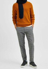 Orange textured sweater, gray checked trousers, and dark sneakers. Accessories include a black scarf. Overall, a layered and casual look.