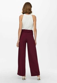 Bordeaux wijde broek met een elastische tailleband, gemaakt van een lichtgewicht materiaal; gecombineerd met een aansluitend wit mouwloos topje.