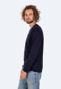 Marineblaues Langarmshirt aus weichem Stoff; verfügt über einen runden Ausschnitt und seitliche Schlitze. Kombiniert mit hellblauen Jeans für einen Kontrast.