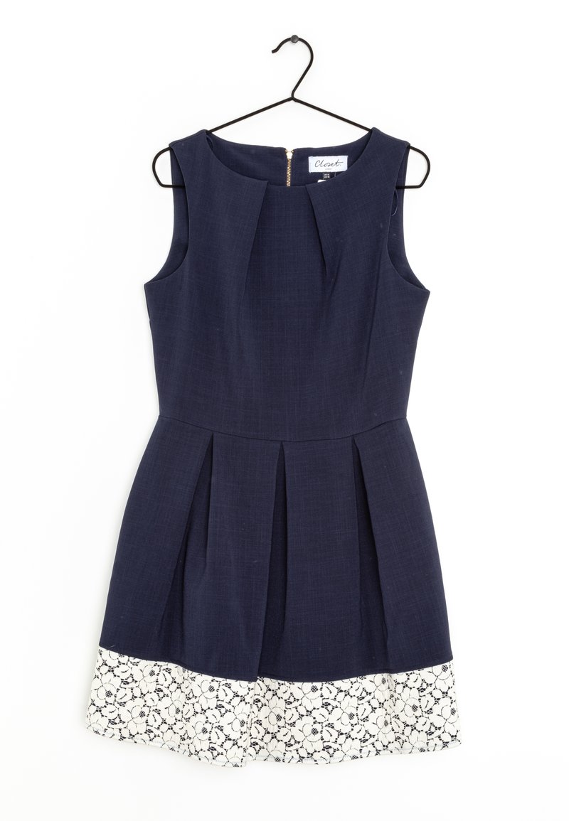 Robe bleu marine sans manches avec plis et bordure en dentelle florale blanche à l'ourlet, suspendue à un cintre métallique noir sur fond blanc.