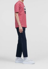 Camiseta roja con estampado y gráfico negro en el pecho, combinada con pantalones oscuros de color marino y zapatillas blancas. Tela suave, ajuste casual.