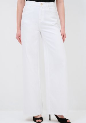 White high-waisted jeans with wide legs, featuring front pockets, a button closure, and a smooth denim texture. Worn with black open-toe heels.