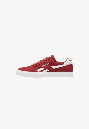 Sneaker bassa rossa Reebok con suola bianca e strisce bianche con logo sul lato, allacciatura frontale e linguetta sul tallone con marchio.