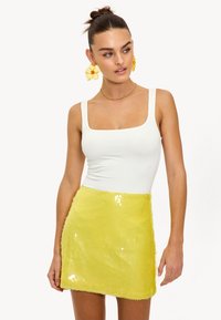 Witte mouwloze top met vierkante halslijn, gecombineerd met een gele minirok met pailletten en een gestructureerde afwerking en gegolfde zoom.