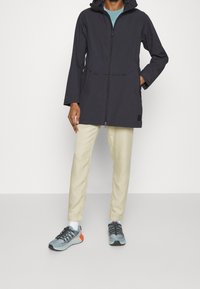 Mustan, vetoketjullinen sadetakki, jossa on huppu, kaksi etutaskua ja rento leikkaus. Yhdistetty vaaleisiin housuihin ja urheiluvaaleisiin kenkiin.