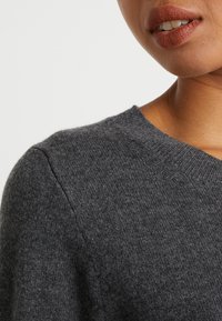 Suéter gris de punto con cuello redondo, que presenta una textura suave y un patrón sutil. Vista en primer plano que resalta los detalles del hombro y el escote.