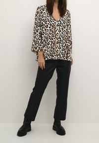 Blusa a fantasia leopardata con scollatura a V e ampie maniche a tre quarti, abbinata a pantaloni neri in ecopelle e stivaletti neri alla caviglia.