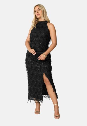 Abito lungo nero con frange e dettagli di perline, scollatura alta e spacco laterale. Abbinato a sandali metallici e una clutch nera.