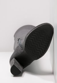 Šedá semišová bota s texturovanou podrážkou, bočním zipem a masivním podpatkem. Podrážka má vlnitý vzor pro lepší trakci.