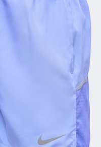 Αθλητική βερμούδα ανοιχτό μωβ με πλαινή διχτυωτή φάσα και ανακλαστικό λογότυπο Nike κοντά στο τελείωμα.