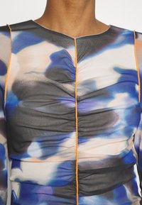 Haut transparent multicolore présentant un mélange de bleus, noirs et pêches avec une texture froncée et des coutures orange le long de l'encolure.