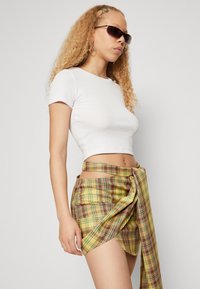 White fitted short-sleeve top paired with a yellow plaid wrap skirt featuring brown and red accents, and a loose tied knot at the waist.