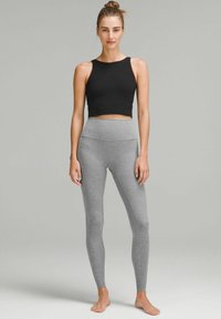 Top corto nero con scollatura ampia abbinato a leggings grigi a vita alta. Entrambi sono lisci e aderenti, progettati per il comfort e il movimento.