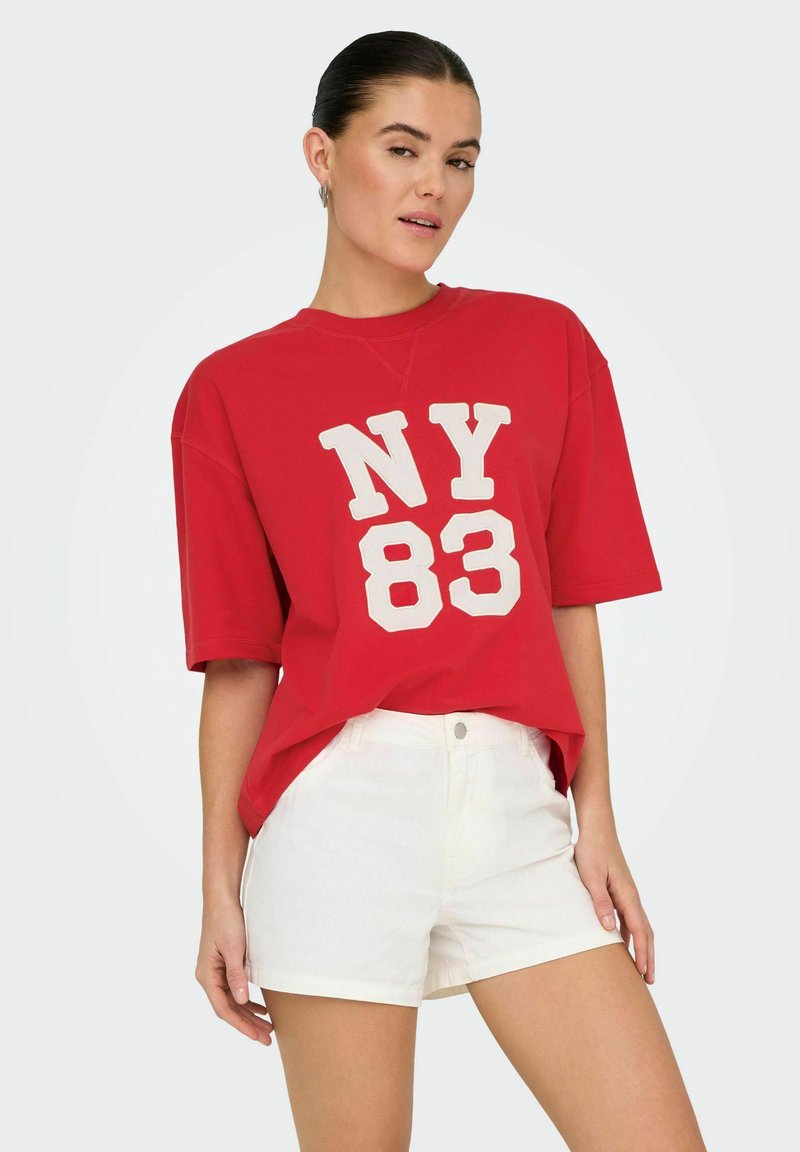Rood oversized t-shirt met witte "NY 83" opdruk, gecombineerd met witte shorts. De stof lijkt zacht met een ontspannen pasvorm en ronde halslijn.