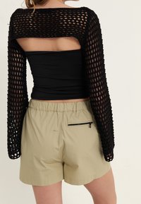 Suéter negro de punto abierto recortado con mangas largas, combinado con pantalones cortos beige claros que cuentan con una cintura elástica y un bolsillo trasero con cremallera.