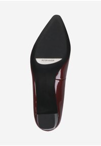 Chaussure à talon aiguille en vernis rouge avec un bout pointu. La semelle comporte un patch en caoutchouc noir et une étiquette métallique avec le nom de la marque.