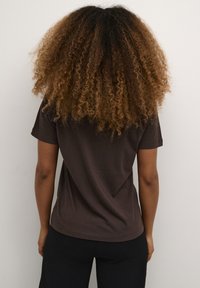 T-shirt corto marrone, realizzato in morbido cotone, con una vestibilità comoda e scollatura rotonda, dalla texture liscia e con dettagli di design minimi.