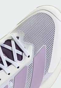 Chaussure de sport gris clair avec une tige en maille, accents violets, lacets blancs et une semelle en caoutchouc lisse. Elle présente un tissu texturé et un col rembourré.