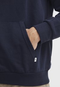 Marine sweatshirt med kengurulomme og ribbede mansjetter. Et bemerkelsesverdig detalj inkluderer et lite hvitt merke på lomme-sømmen. Stoff i bomullsblanding.