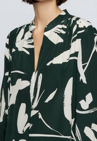 Blouse verte avec un imprimé floral abstrait en crème, sans col, à coupe décontractée et en tissu doux.