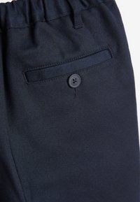 Dunkelblaue Hose aus strukturiertem Stoff, mit elastischem Taillenbund und einer Gesäßtasche mit schwarzem Knopfverschluss.