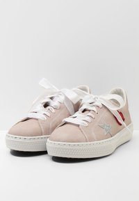 Jasnoróżowe trampki z płóciennej tkaniny z białymi gumowymi podeszwami, zdobione metaliczną srebrną gwiazdą i czerwonym łatą, sznurowane bia�łymi sznurówkami.