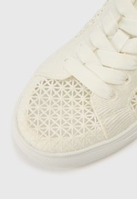 Fehér sportcipő texturált szövet felsőrésszel, geometriai mintával és lapos fűzőkkel. Kiemelt gumitalp fokozza a tapadást.